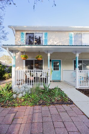 A two-story house with a blue door and white shutters, a front porch with white railings, and hanging flower baskets.