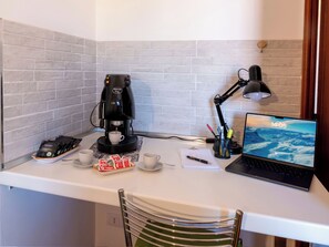 Et arbejdsområde med kaffemaskine, laptop, skrivebordslampe og en computerskærm, der viser et bjerglandskab.