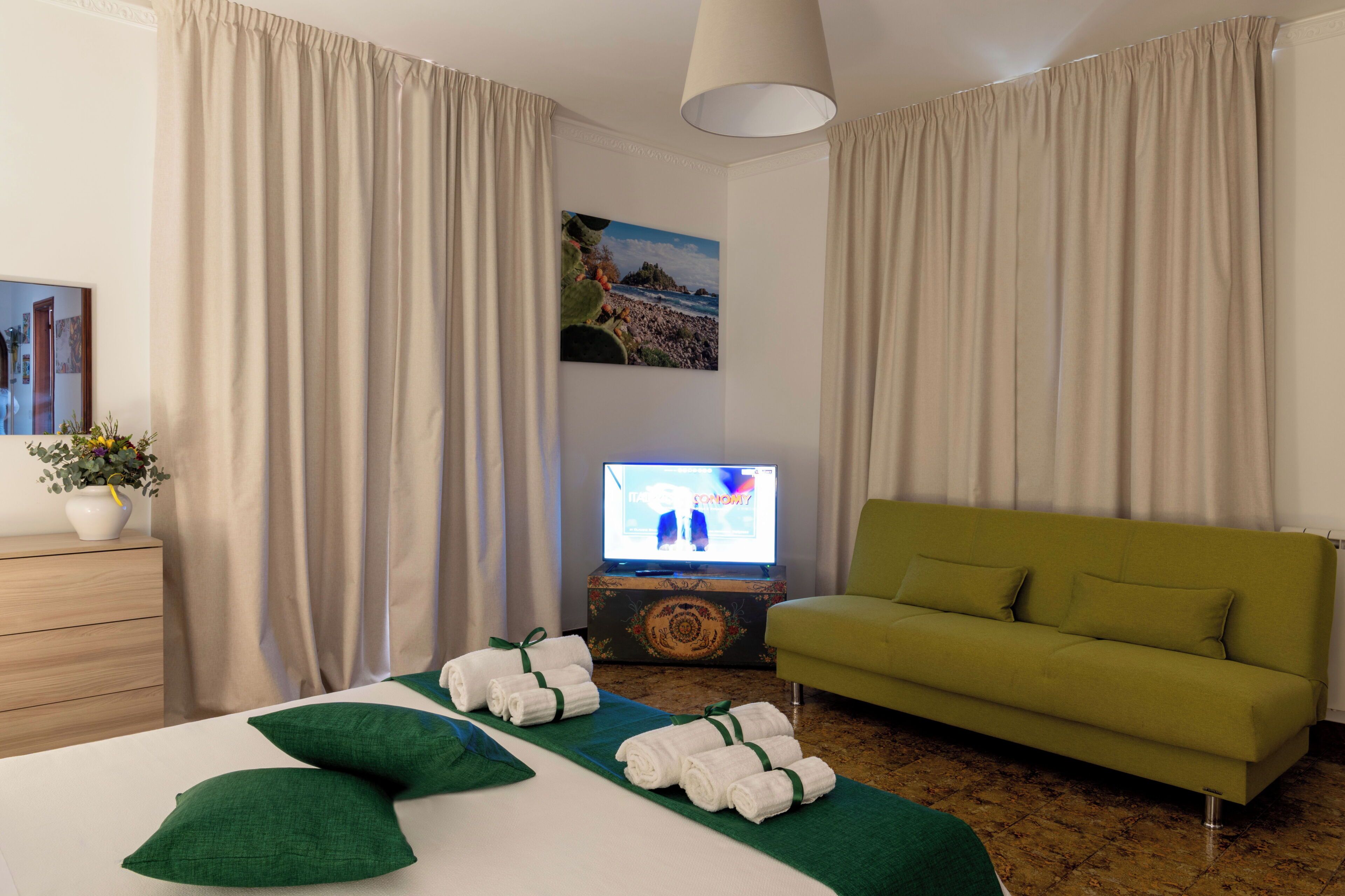 Una camera d'albergo con un letto, un divano verde, una televisione e un quadro appeso al muro.