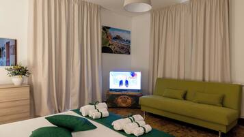 Una camera d'albergo con un letto, un divano verde, una televisione e un quadro appeso al muro.
