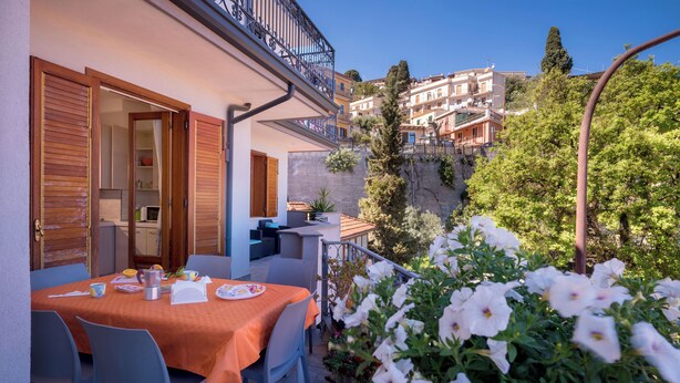 Eine Terrasse mit Esstisch, ein Balkon mit Geländer und Blick auf Gebäude im Hintergrund.