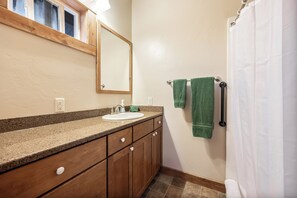 Une salle de bain avec un lavabo sur un plan de travail en granit, des meubles en bois, un miroir et un rideau de douche.