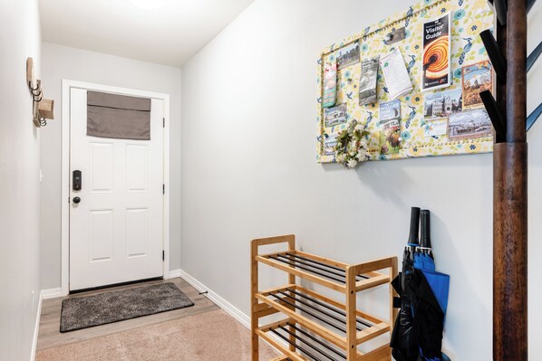 A hallway with a white door, a bulletin board with various photos and notes, and a wooden rack with umbrellas. - The Sizzl-INN' Seagull (Olympia)