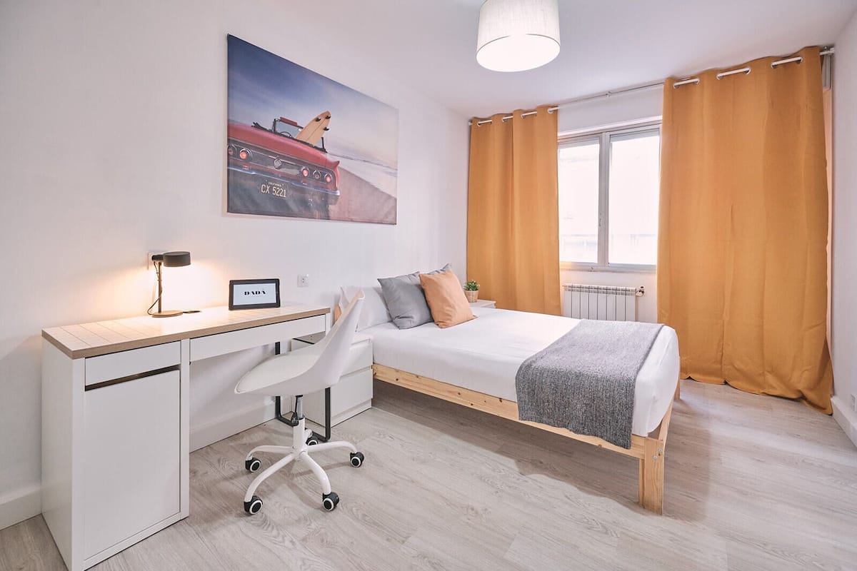 Een moderne slaapkamer met een houten bed, wit bureau en bureaulamp.