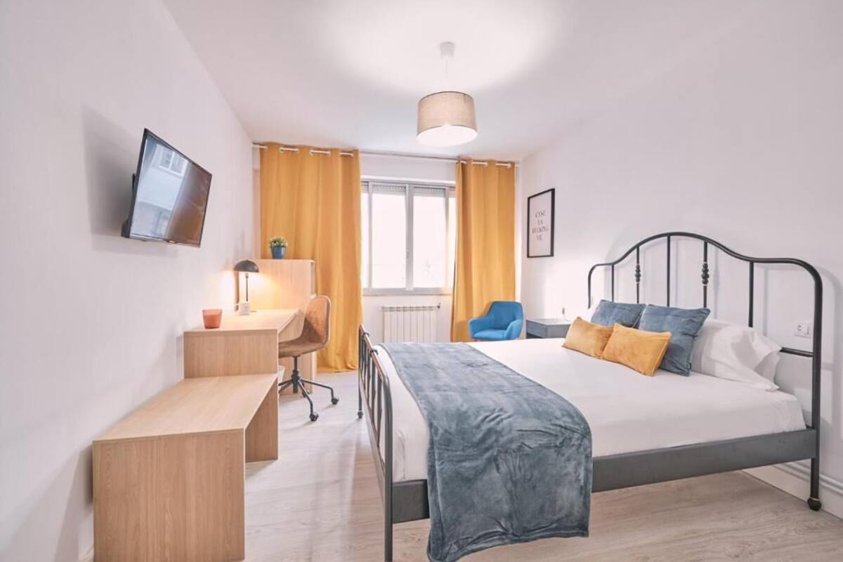 Een slaapkamer met een bed, een bureau, een stoel, een televisie en een raam met gordijnen.