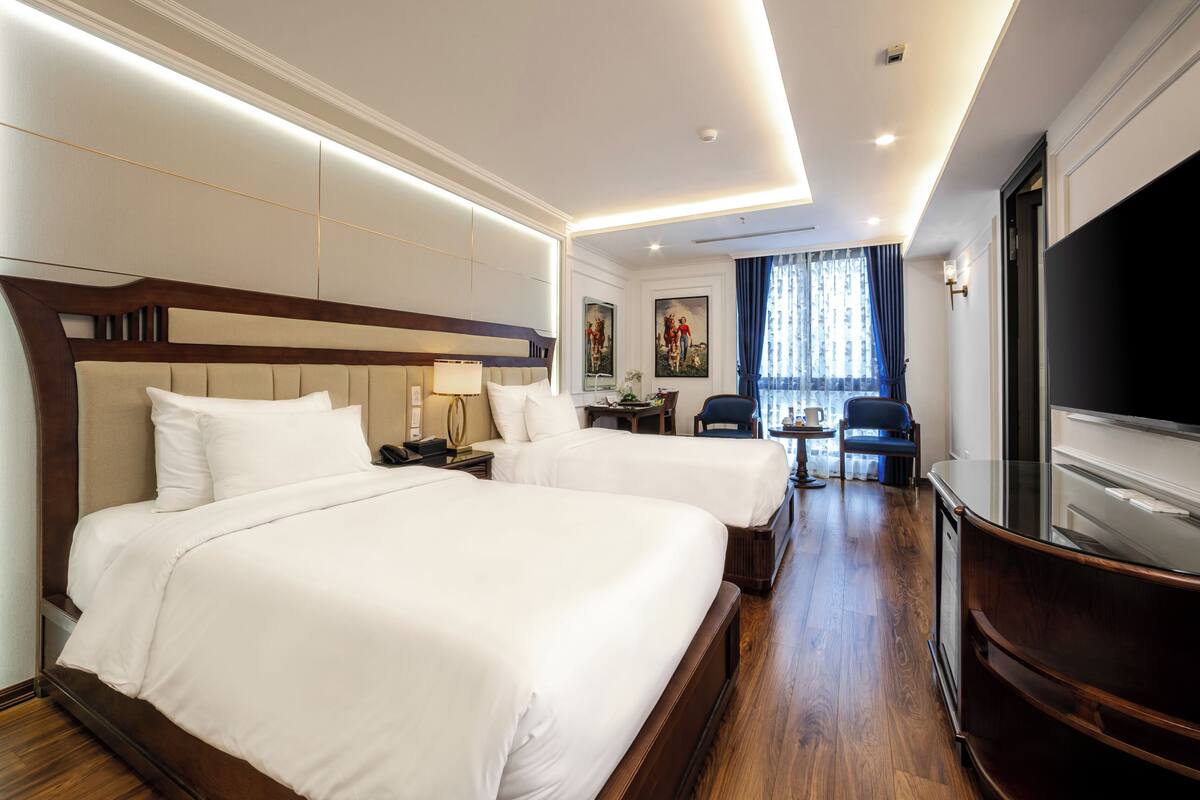 A hotel room with two beds, a TV, a desk, and a chair.