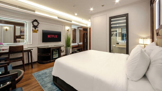 Une chambre d’hôtel avec un grand lit, un téléviseur fixé au mur, un bureau avec une chaise, une plante en pot et un miroir.