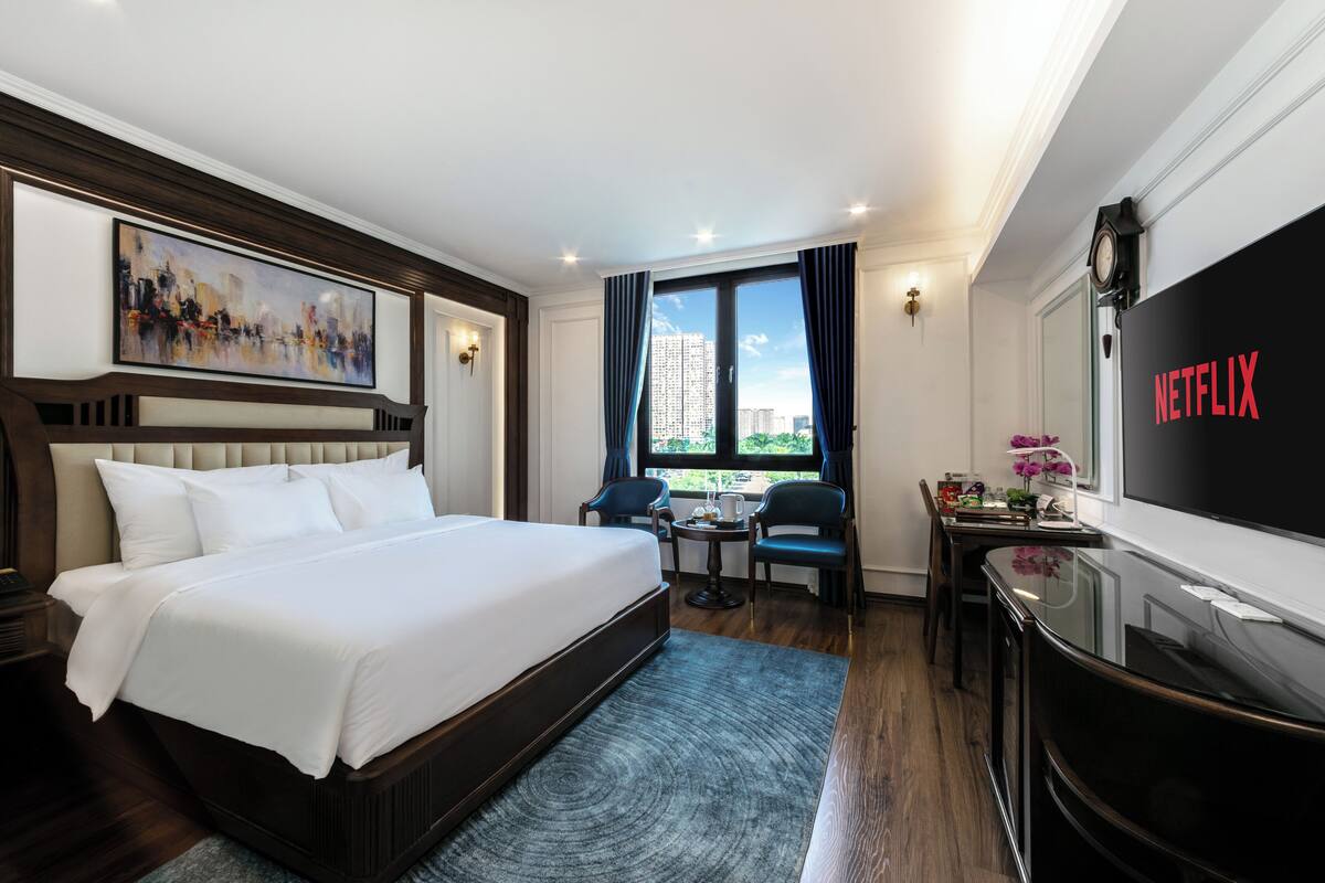 A hotel room with a large bed, a desk with a computer, a TV, and a window with curtains.