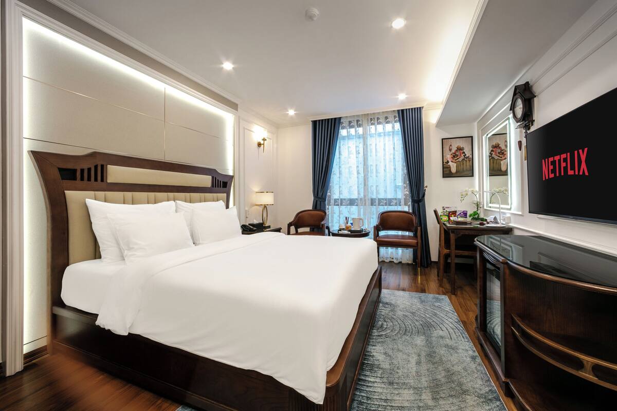 A hotel room with a large bed, a desk with a chair, a television, and a clock on the wall.