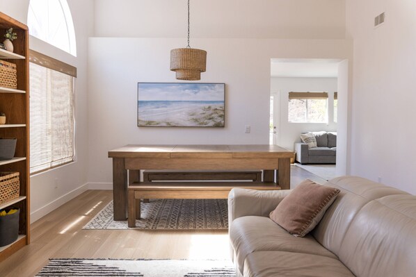 Un salon moderne avec un banc en bois, un canapé beige, un luminaire suspendu en fibres tressées et un tableau représentant un paysage, encadré et accroché au mur.