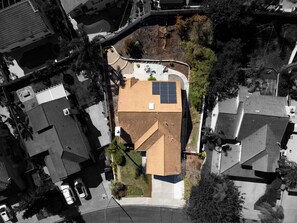 An aerial view of a residential area with a house featuring a sloped roof, solar panels, and a small garden. - Fresh, Clean, Relaxing Home, in the Heart of North County San Diego (San Marcos)