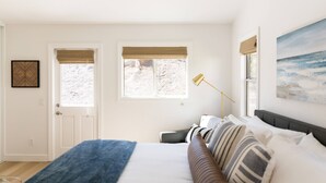 Une chambre à coucher avec un lit, deux fenêtres équipées de stores, une lampe sur pied et un tableau accroché au mur.