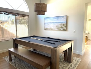 Une table de billard avec les queues, un luminaire en fibres tressées et un tableau représentant une scène de plage.