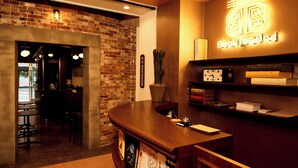 Un coin bar accueillant avec un comptoir en bois, un panneau néon indiquant « BookTeaBed » et une horloge au mur.