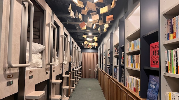 Un couloir d’hôtel avec des lits superposés d’un côté et une bibliothèque remplie de livres de l’autre.