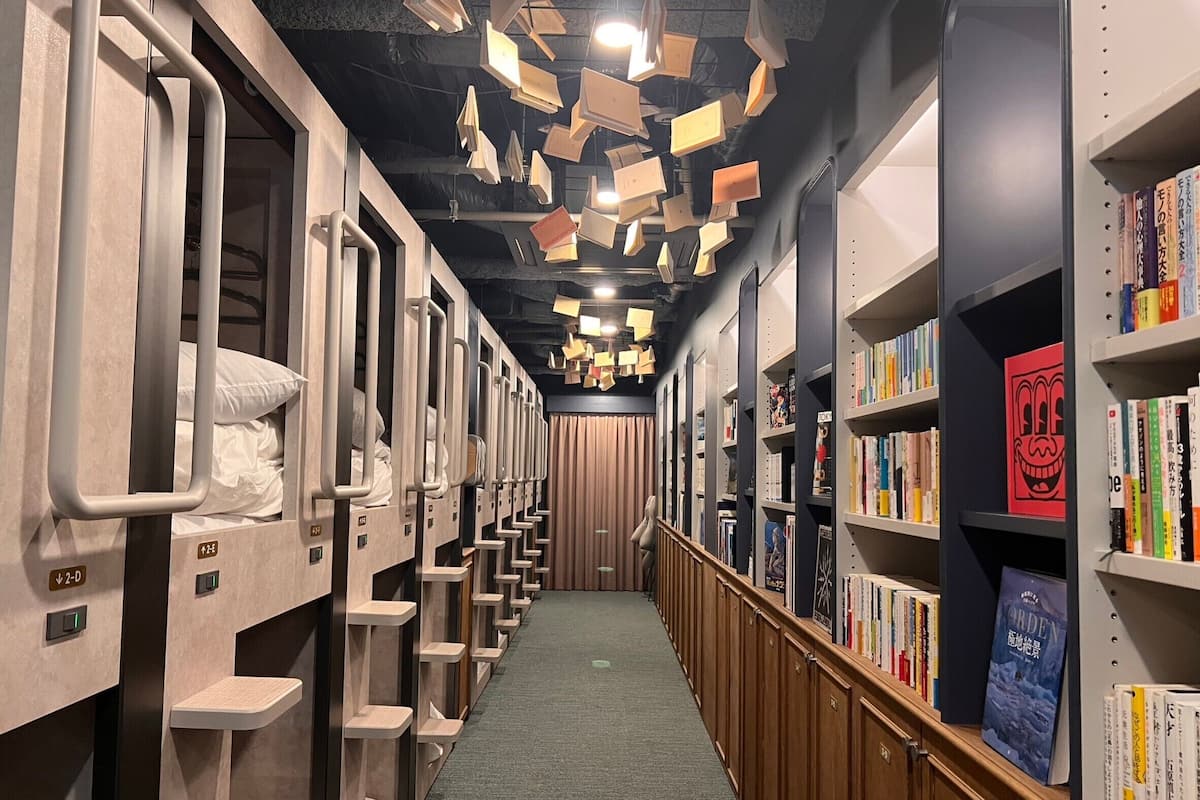 A hotel corridor with bunk beds on one side and a bookshelf filled with books on the other.