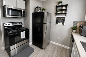 A modern kitchen with stainless steel appliances, a black refrigerator, and a welcome sign on the wall. - Cozy, Contemporary Haven Near Historic Downtown (Savannah)