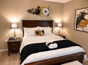 A hotel room with a large bed, two bedside tables with lamps, a wall clock, and a decorative wall piece. - Cozy, Contemporary Haven Near Historic Downtown (Savannah)