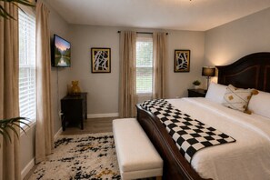 A bedroom with a large bed, a bedside table, a lamp, and a window with curtains.