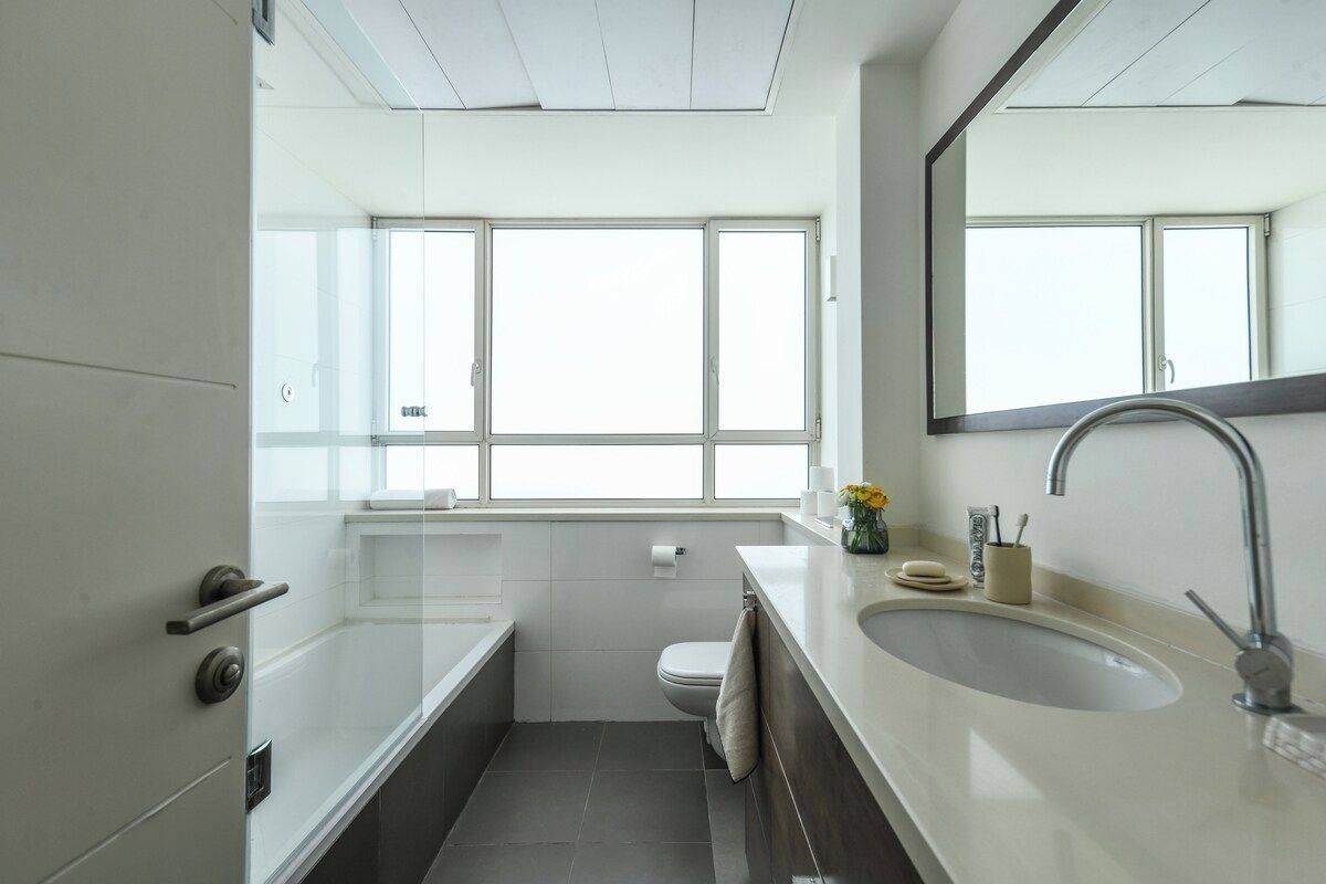Ein modernes Badezimmer mit einem großen Fenster, einer Badewanne, einer Toilette und einem Waschbecken mit Spiegel.