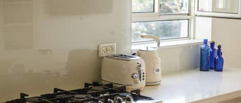 A kitchen with a gas stove, a toaster, and a window with a view of greenery outside.