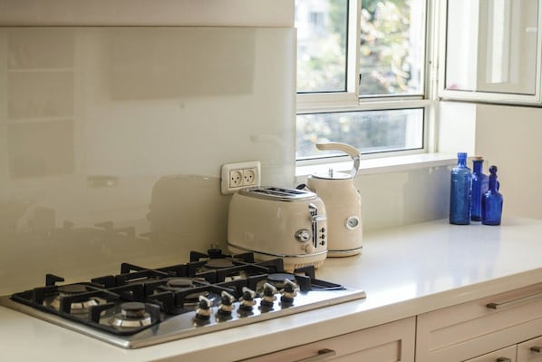 A kitchen with a gas stove, a toaster, and a window with a view of greenery outside.