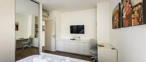 A hotel room with a bed, a desk, a chair, a television, and artwork on the wall.