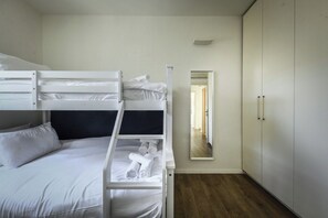 A bunk bed with white bedding and towels, a wardrobe, and a mirror reflecting a hallway.