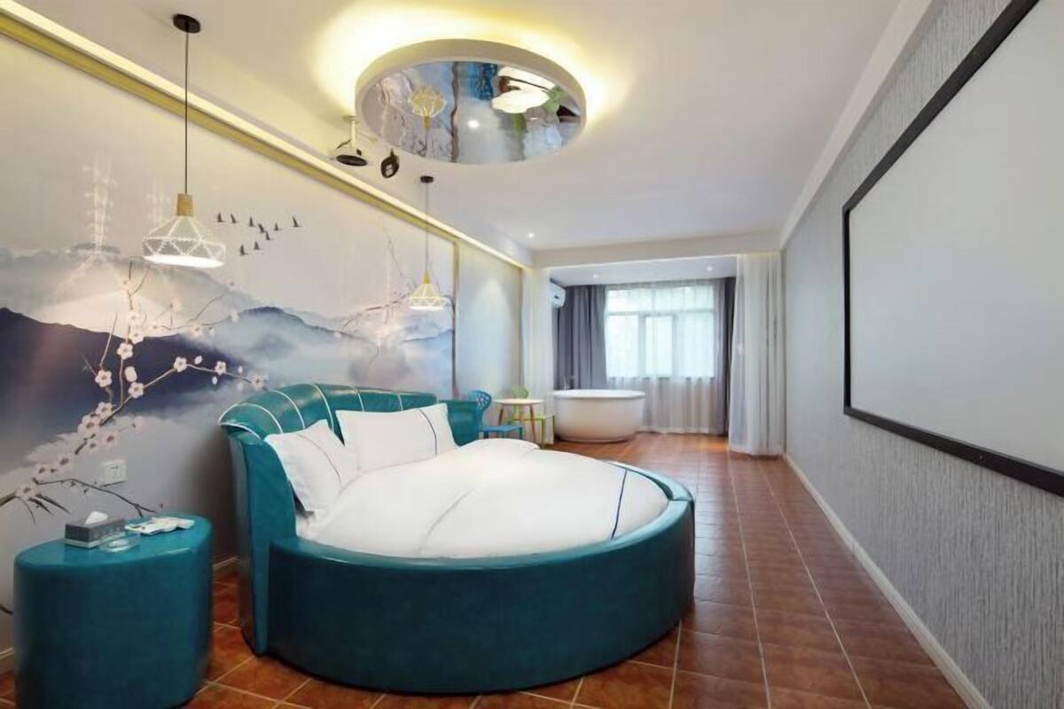 Un dormitorio moderno con una cama redonda, un mural en la pared y una lámpara de techo circular.