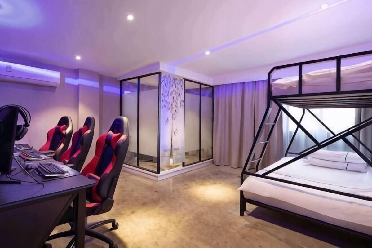 Habitación de hotel con literas, un escritorio con computadoras y un muro divisorio de vidrio.