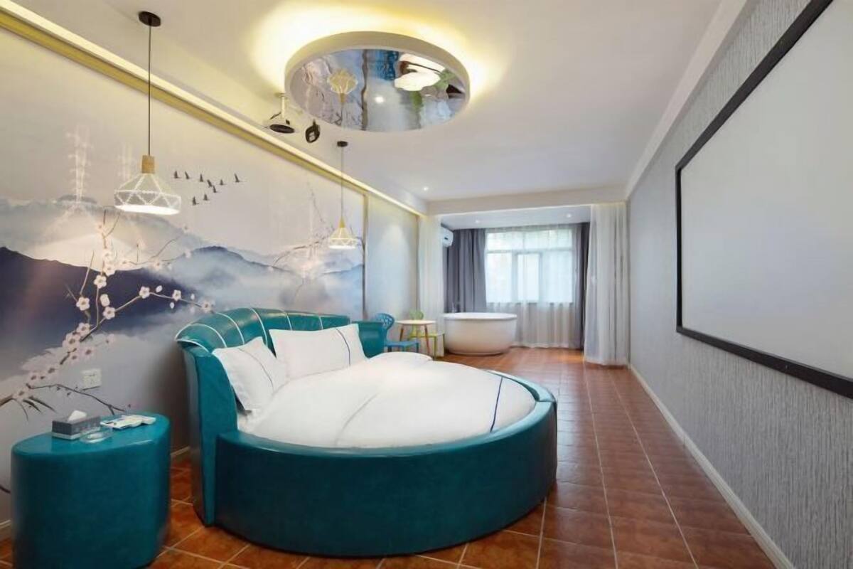 Un dormitorio moderno con cama redonda, un mural en la pared y una lámpara de techo circular.