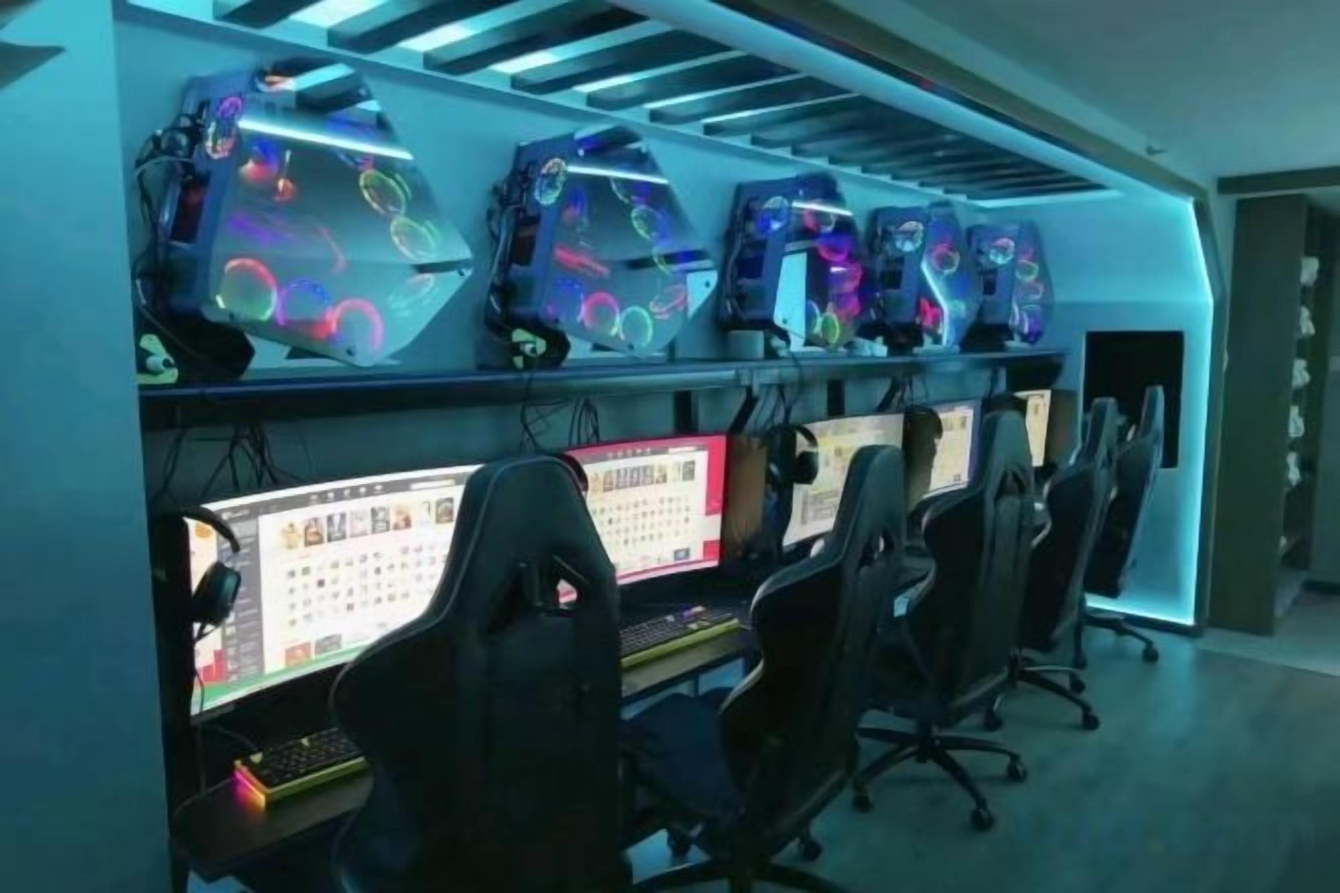A gaming room with multiple gaming stations, chairs, and illuminated gaming PCs.