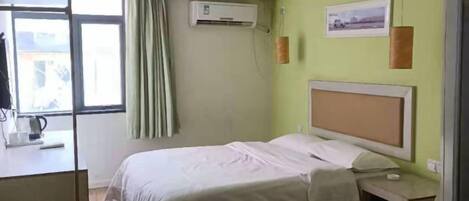 A hotel room with a bed, bedside table, and a window with curtains.