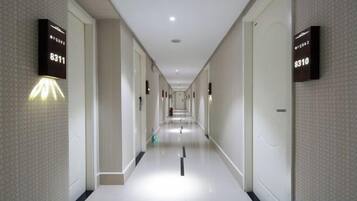 Un pasillo de hotel con números de habitación iluminados en las paredes, piso de baldosas limpias y un camino recto hasta el final del pasillo.
