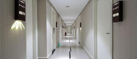 A hotel corridor with illuminated room numbers on the walls, a clean tiled floor, and a straight path leading to the end of the corridor.