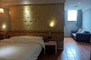 Una habitación de hotel con una cama grande, un sofá, una mesita de noche y una lámpara de pared.