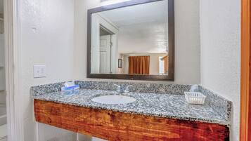 A bathroom with a granite countertop sink, wooden vanity, and a large mirror.