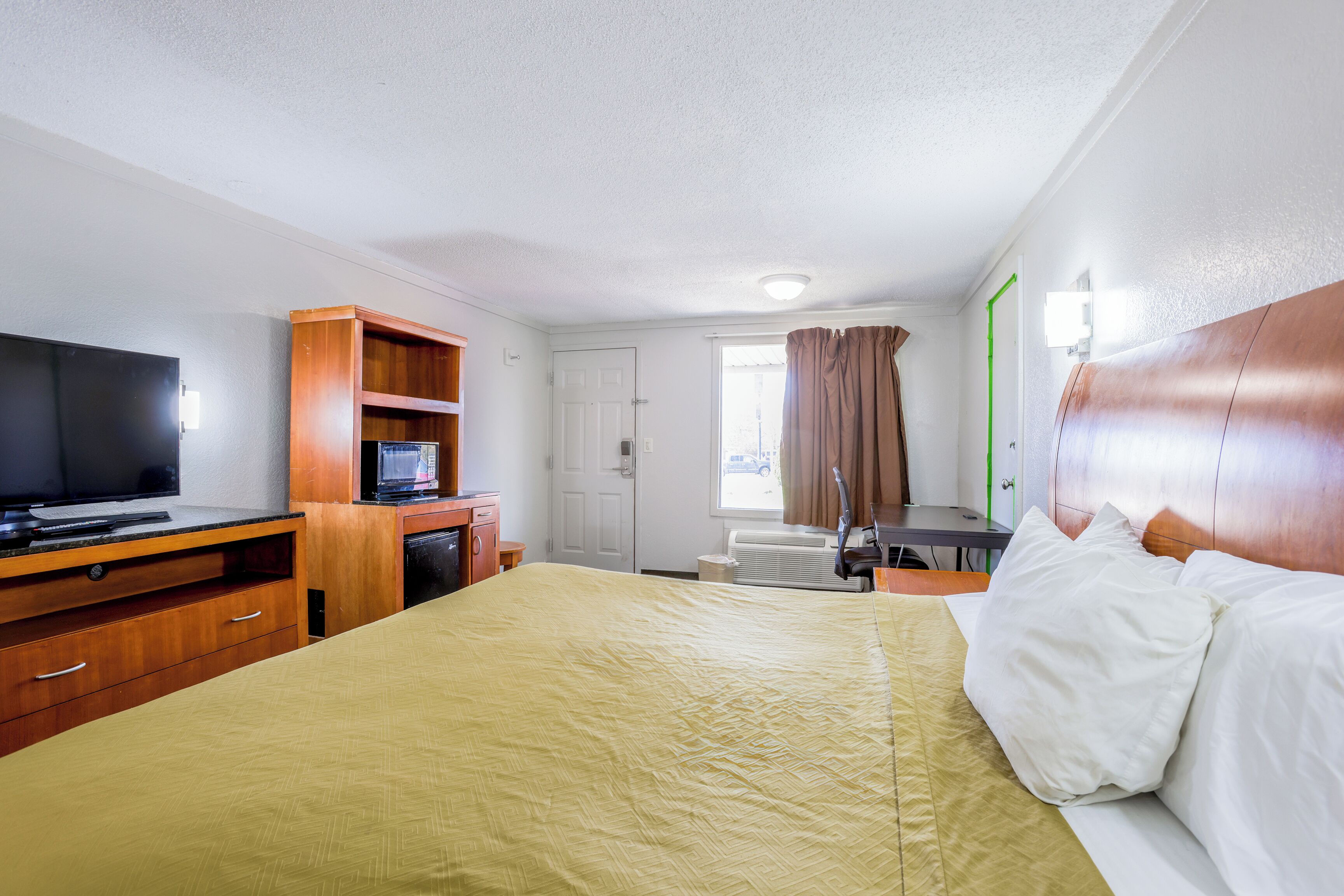 Ein Hotelzimmer mit Bett, Fernseher, Schreibtisch und einem Fenster mit Vorhängen.
