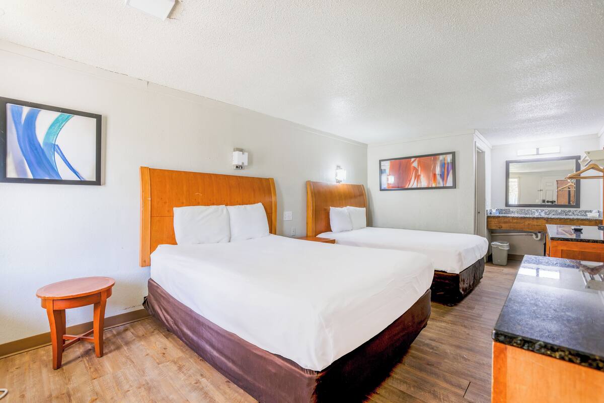 A hotel room with two beds, a small table, a mirror, and a bathroom.