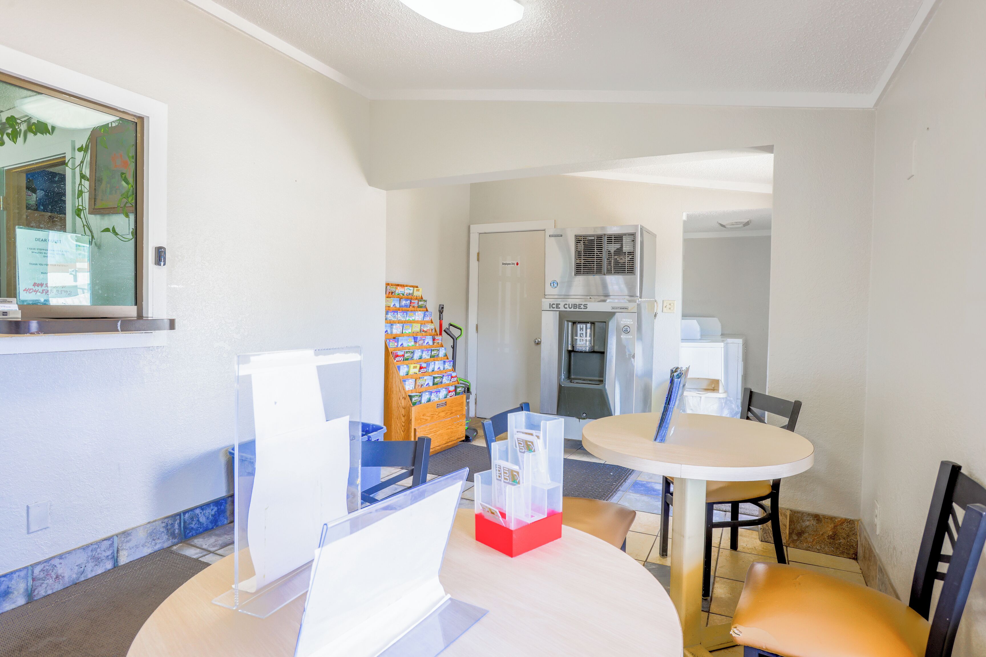 Una habitación pequeña y limpia con una mesa redonda, sillas, un refrigerador y una máquina expendedora.