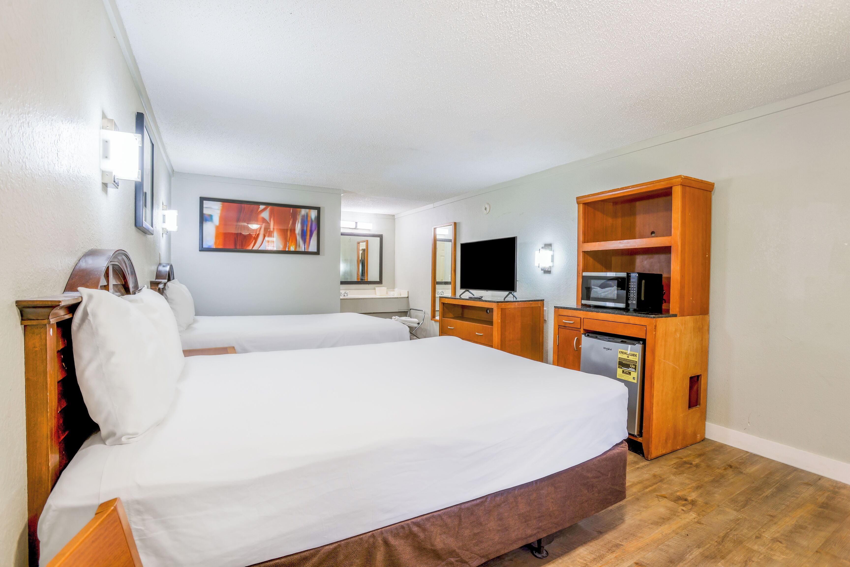 A hotel room with two beds, a wooden cabinet with a microwave, a TV, and a small refrigerator.