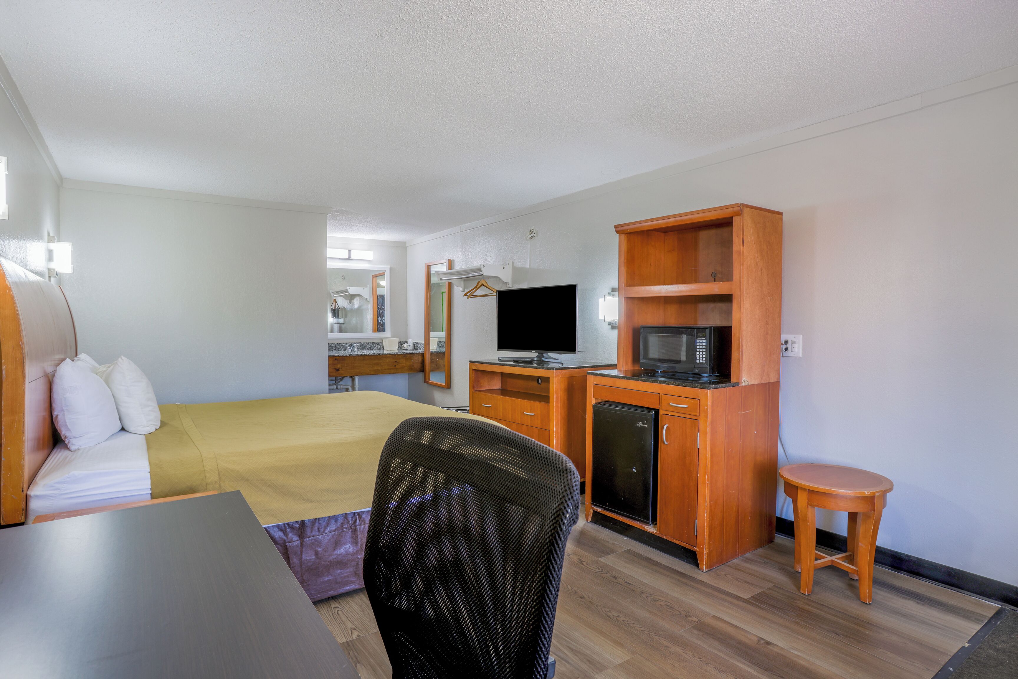 A hotel room with a bed, a desk, a chair, a TV, a microwave, and a small cabinet.