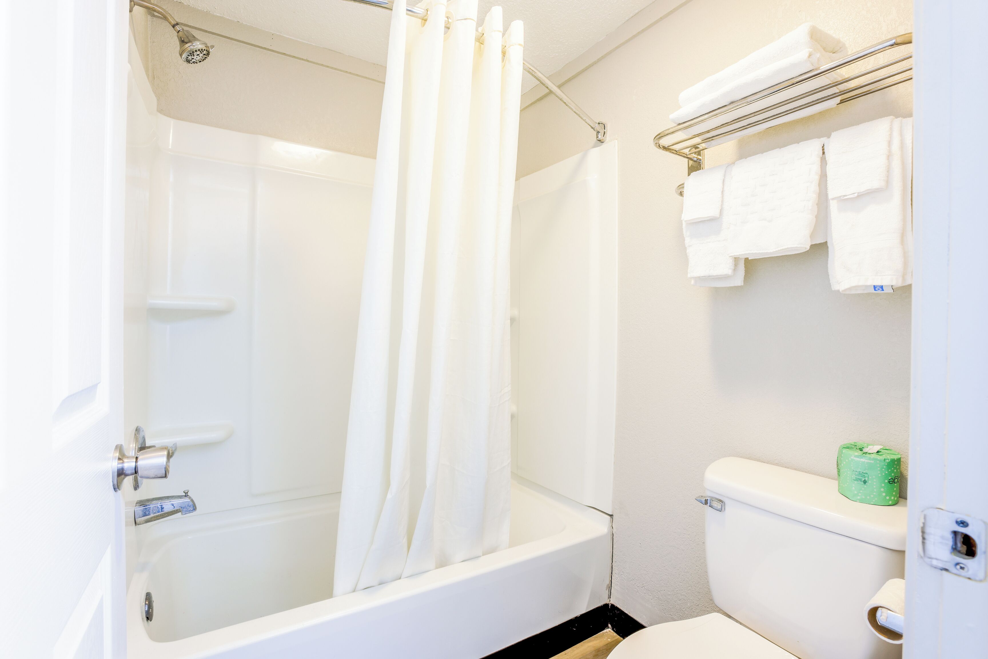 A bathroom with a bathtub, shower curtain, toilet, and towel rack.