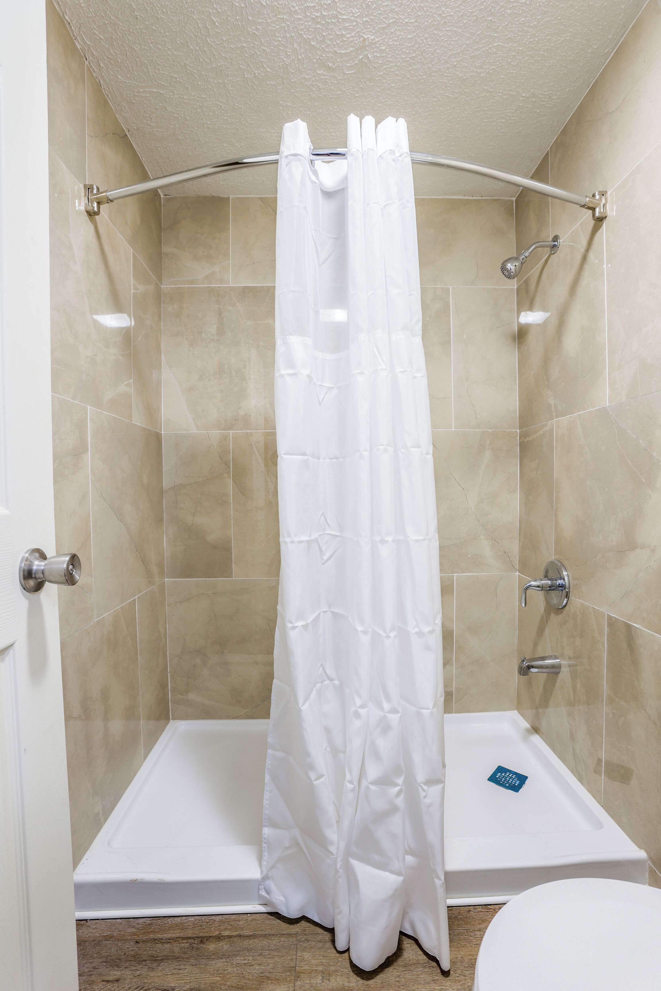 A shower with a white curtain, a handheld showerhead, and a handheld faucet.
