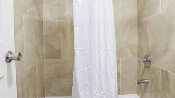 A shower with a white curtain, a handheld showerhead, and a handheld faucet.