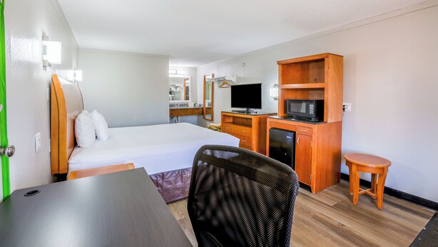 Ein Hotelzimmer mit Bett, Schreibtisch, Stuhl, Fernseher, Mikrowelle und einem kleinen Tisch.
