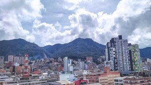 Paisagem urbana com um edifício moderno de destaque e fachada singular, rodeado por edifícios residenciais e comerciais, sob um céu nublado.