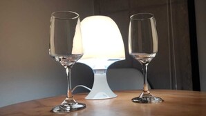 Duas taças de champanhe sobre mesa de madeira, com um abajur branco ao fundo.