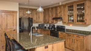 Cocina con armarios de madera, encimeras de granito, electrodomésticos de acero inoxidable e iluminación colgante.