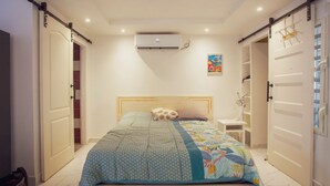Een slaapkamer met een bed, nachtkastje, airconditioning en een deur met schuivmechanisme.